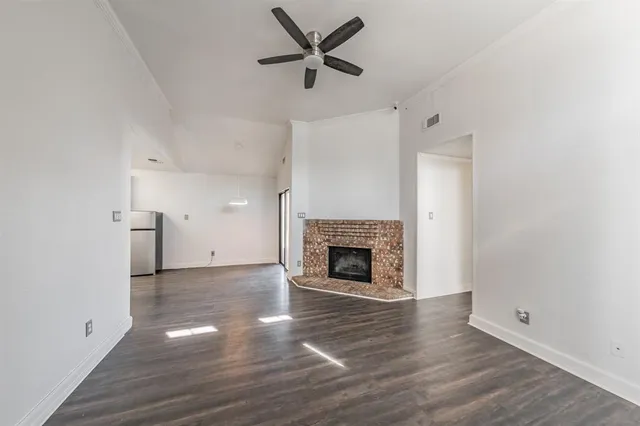 an empty room with wooden floor a ceiling fan a fireplace and windows
