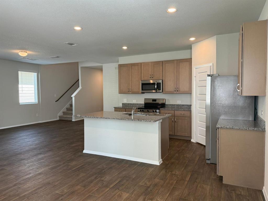 2707 Totley Road Pflugerville, TX 78660 - Photo 9 of 39 Kitchen featuring light stone countertops, stainless steel appliances, an island with sink, dark wood-style floors, and recessed lighting