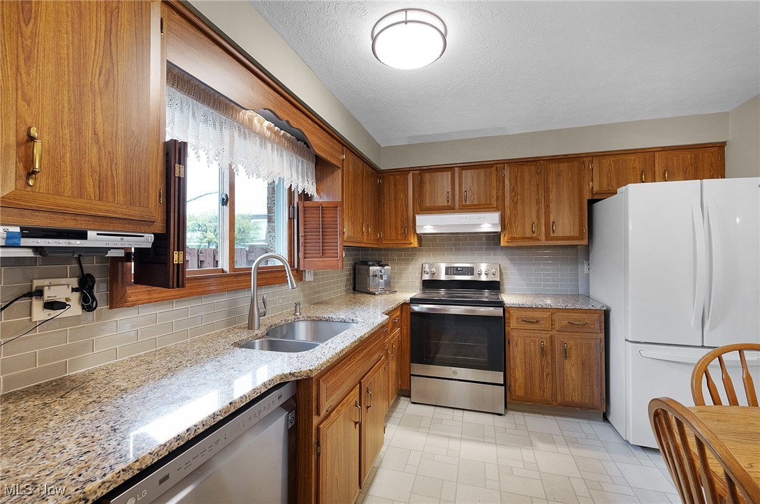 6474 State Road, Unit I10 Parma, OH 44134 - Photo 4 of 31 Kitchen featuring appliances with stainless steel finishes, brown cabinets, tasteful backsplash, light stone countertops, and a textured ceiling