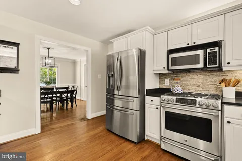 a kitchen with stainless steel appliances granite countertop a stove a sink and white cabinets with wooden floor