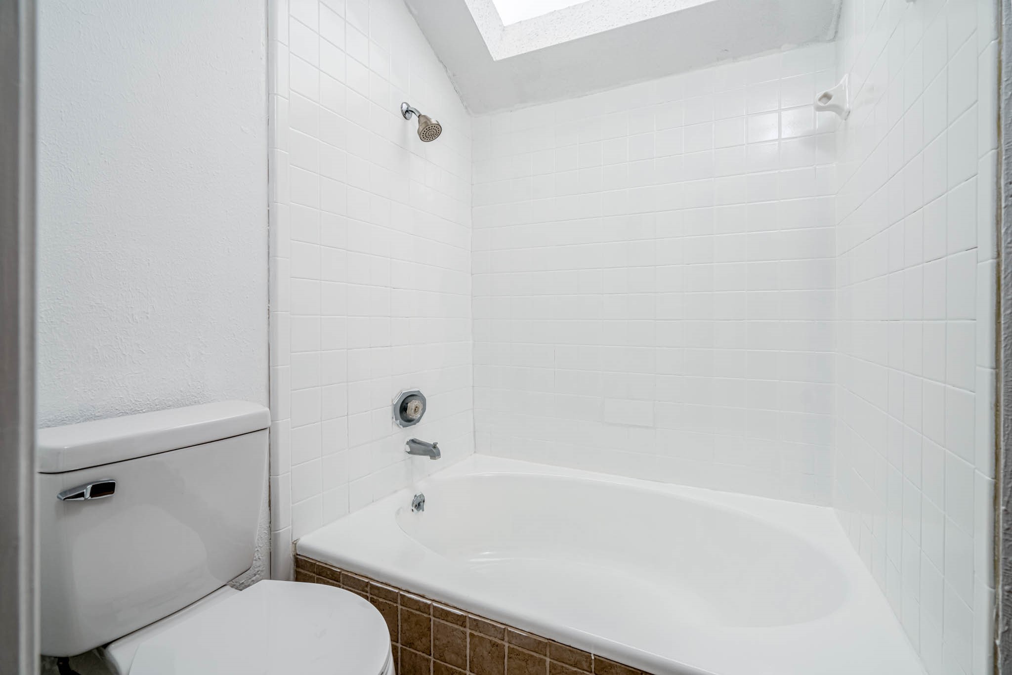 2277 South Kirkwood Road, Unit 4/808 Houston, TX 77077 - Photo 9 of 23 Primary bath, featuring a pristine white tub and shower combo beneath a skylight that bathes the space in natural light.
