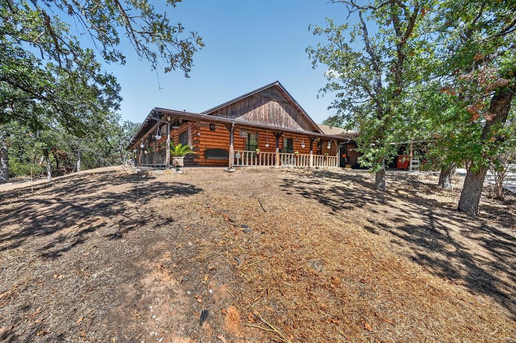 1623 3 Skillet Road Springtown, TX 76082 - Photo 33 of 40 Log cabin exterior with an expansive covered front porch, gabled roofline, and mature trees