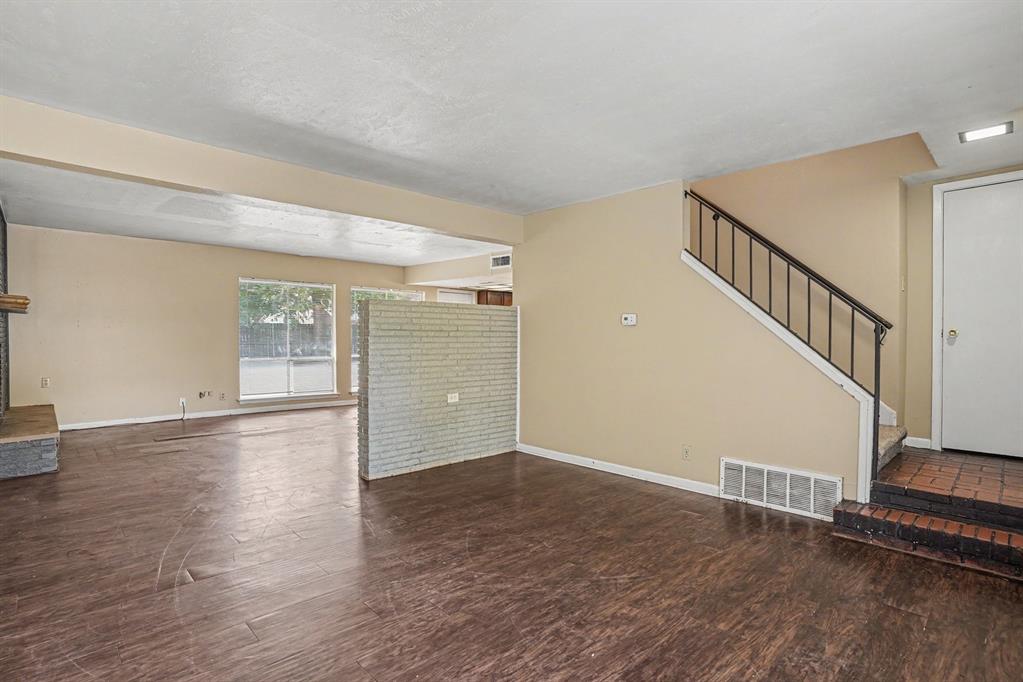 1414 Finley Road Irving, TX 75062 - Photo 4 of 27 Wood-finish flooring throughout, brick accent partition, fireplace with stone surround, large window with outdoor visibility, and a staircase with wrought iron railing