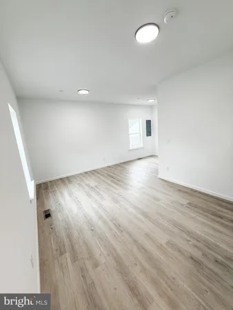 a view of empty room with wooden floor and kitchen