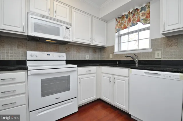 a kitchen with granite countertop white cabinets white appliances and a window