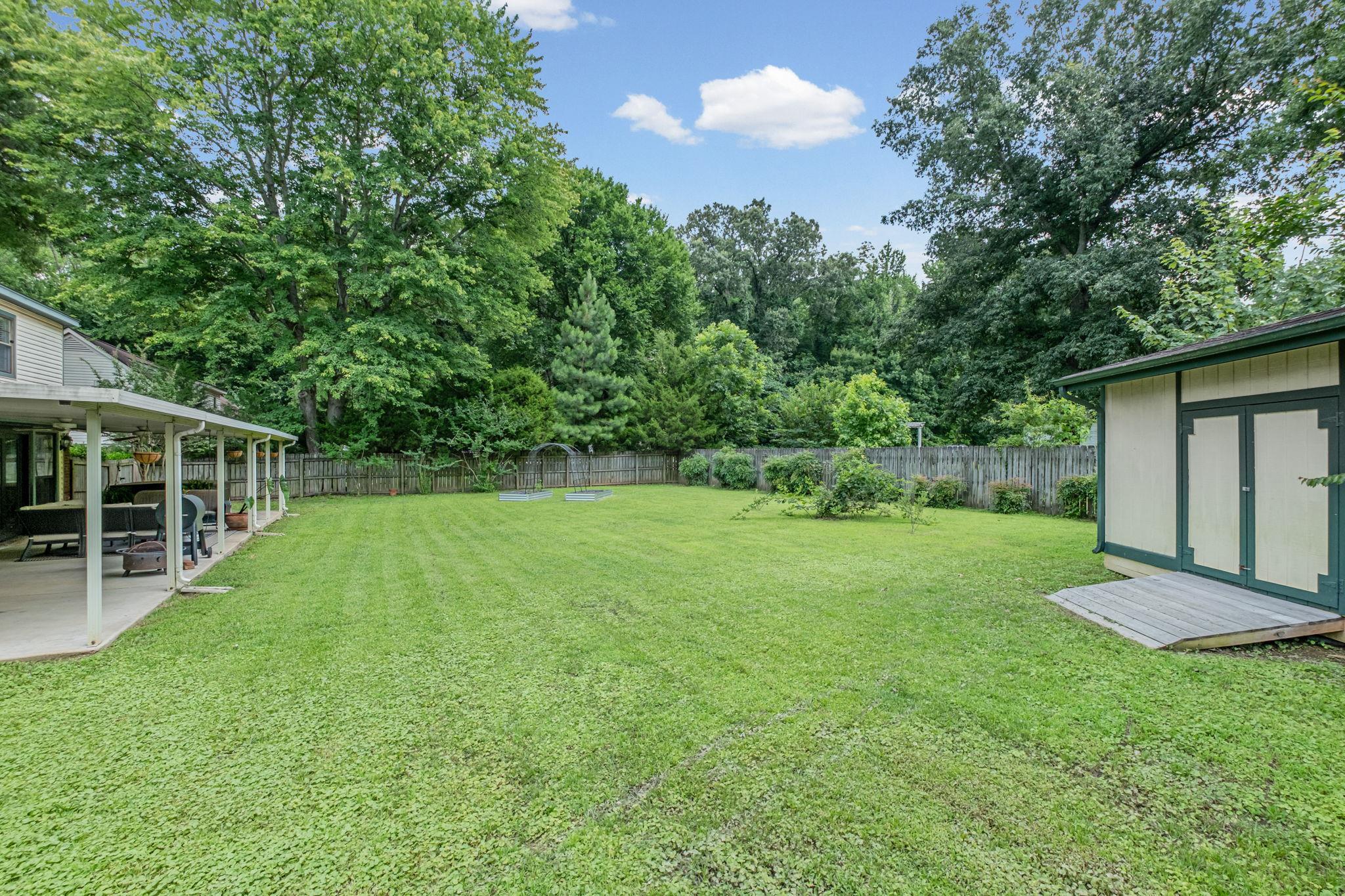 4729 Cedar Ridge Drive Millington, TN 38053 - Photo 36 of 40 Expansive green lawn featuring a covered patio, a storage shed with a ramp, and a perimeter fence, bordered by mature trees
