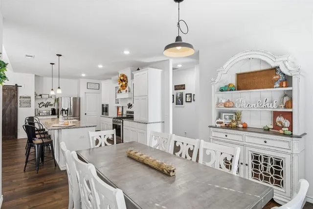 a kitchen with granite countertop a stove a sink a refrigerator and a dining table with wooden floor