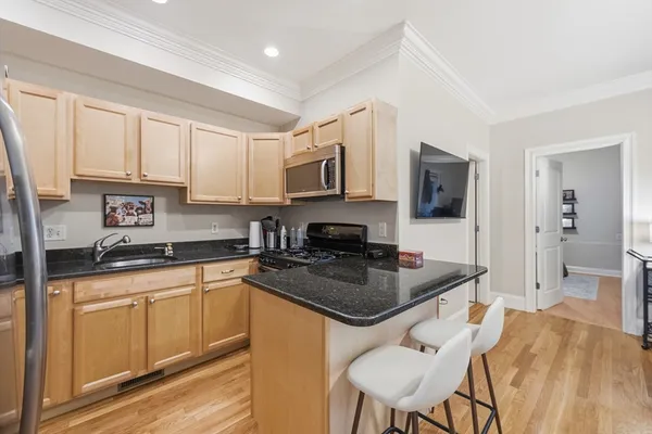 a kitchen with stainless steel appliances granite countertop a stove top oven a sink a refrigerator white cabinets and a chairs with wooden floor