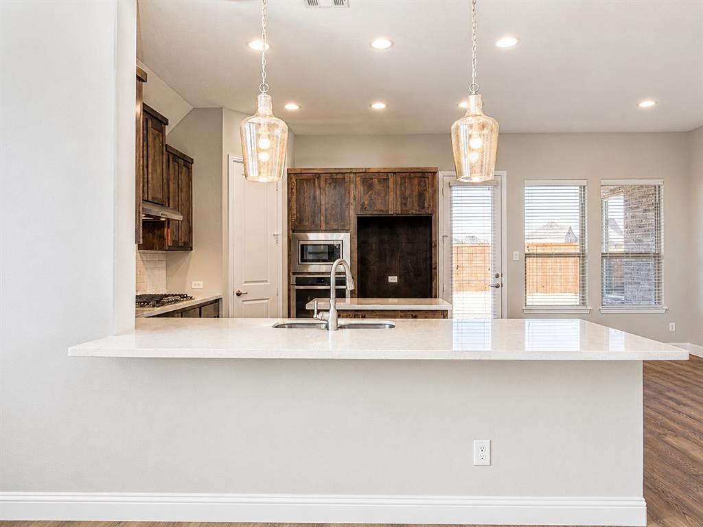 6209 Cupleaf Road Flower Mound, TX 76226 - Photo 10 of 29 Kitchen featuring a built-in stainless steel microwave and oven, dark wood cabinetry, white countertops, and a kitchen island with an integrated sink and gooseneck faucet