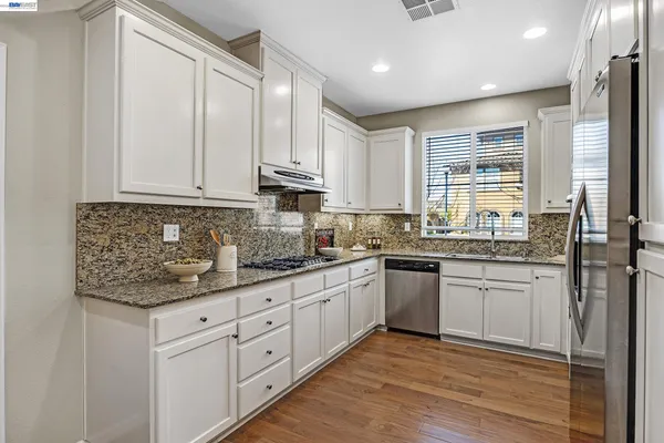 a kitchen with granite countertop white cabinets stainless steel appliances a sink and a window