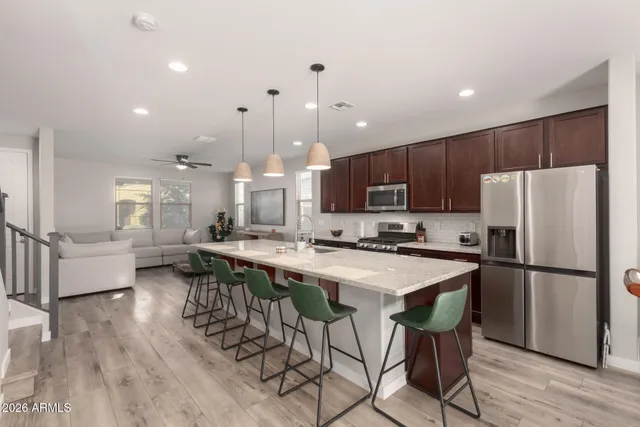 a kitchen with stainless steel appliances a refrigerator a stove a sink a dining table and chairs with wooden floor