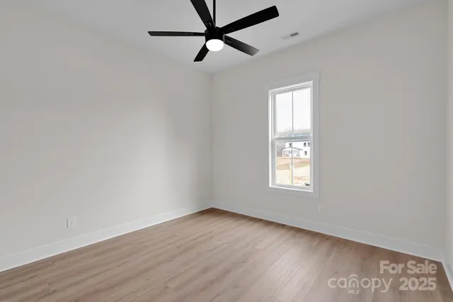 an empty room with wooden floor ceiling fan and windows
