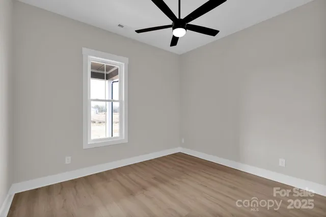 an empty room with wooden floor fan and windows