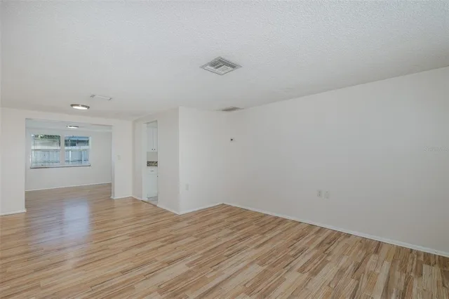 a view of empty room with wooden floor and kitchen