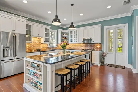 a kitchen with stainless steel appliances granite countertop a stove top oven a refrigerator a dining table and chairs with wooden floor