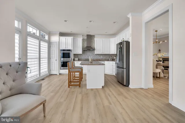 a kitchen with stainless steel appliances a refrigerator a sink dishwasher a stove top oven a dining table and chairs with wooden floor