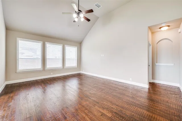 an empty room with wooden floor chandelier fan and windows