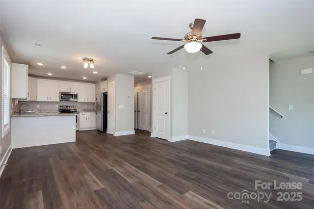 a view of an empty room and kitchen view with wooden floor