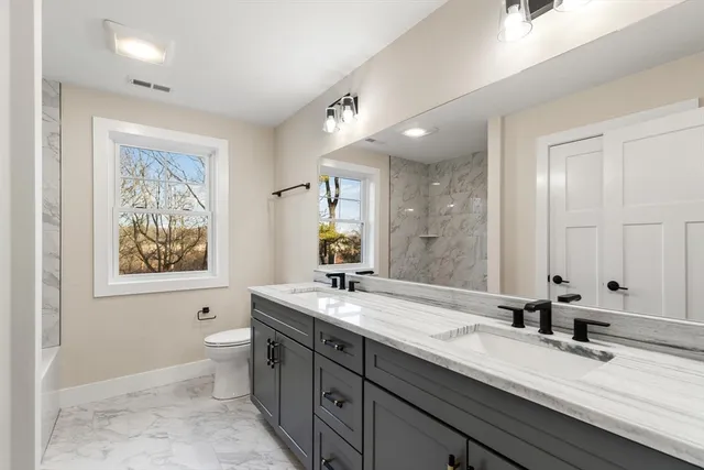 a bathroom with a double vanity sink a large mirror a toilet and a bathtub