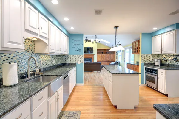 a kitchen with stainless steel appliances granite countertop wooden cabinets a sink dishwasher a stove and a kitchen island with wooden floor