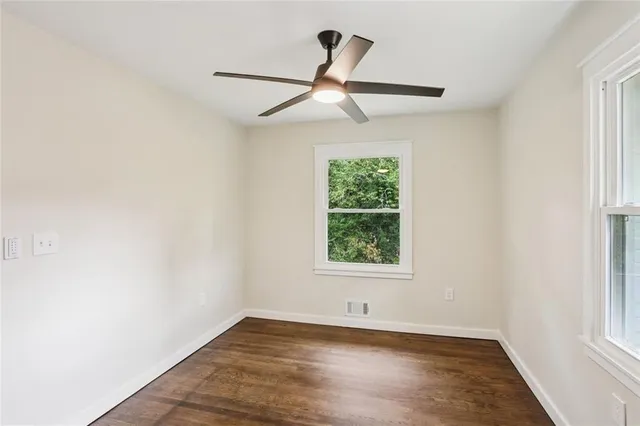 an empty room with wooden floor ceiling fan and windows
