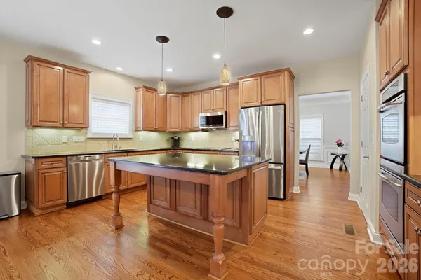 a kitchen with stainless steel appliances granite countertop a refrigerator a sink dishwasher a oven with white cabinets and wooden floor