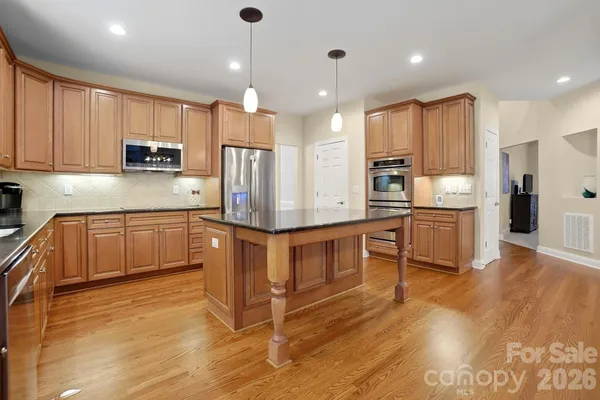 a kitchen with stainless steel appliances kitchen island granite countertop a refrigerator a stove top oven a sink and cabinets