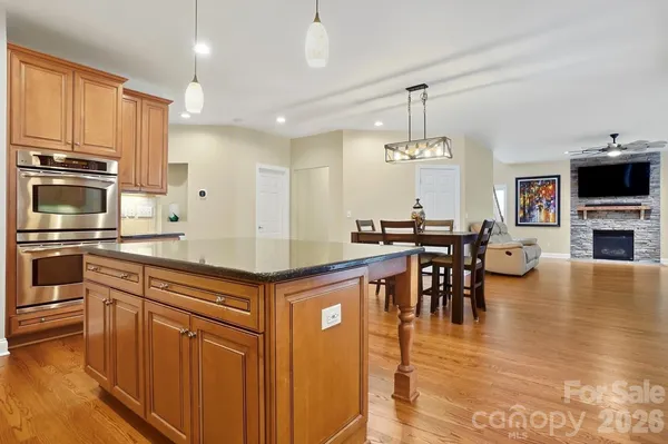 a kitchen with stainless steel appliances granite countertop a stove top oven a refrigerator a dining table and chairs with wooden floor