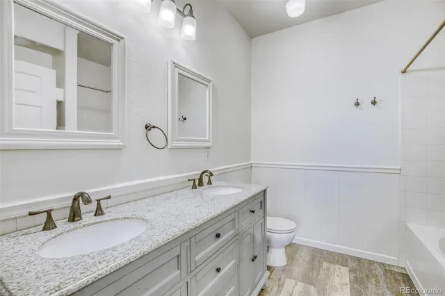 a bathroom with a granite countertop double vanity sink a mirror and a toilet