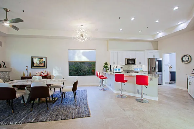 a kitchen with stainless steel appliances kitchen island granite countertop a dining table chairs sink and white cabinets