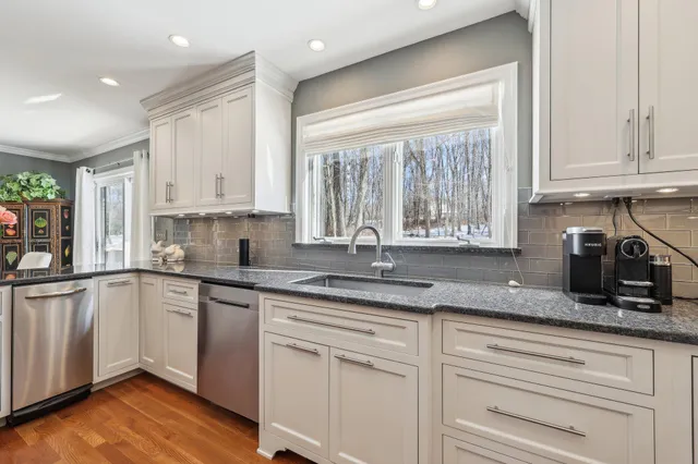 a kitchen with granite countertop stainless steel appliances white cabinets and a window