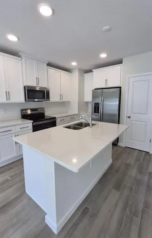 a large kitchen with stainless steel appliances granite countertop a stove a refrigerator a sink and white cabinets with wooden floor