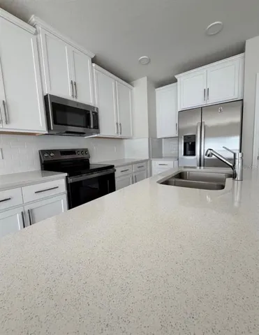 a kitchen with granite countertop a refrigerator a stove a sink and white cabinets