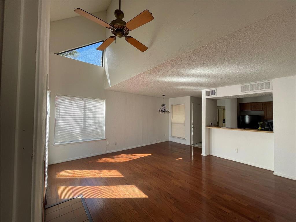 9811 Walnut Street, Unit F207 Dallas, TX 75243 - Photo 1 of 12 Unfurnished living room with dark wood-style floors, a ceiling fan, a high textured ceiling, and a chandelier