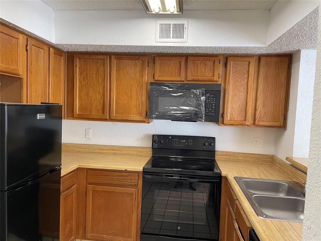 9811 Walnut Street, Unit F207 Dallas, TX 75243 - Photo 12 of 12 Kitchen with black appliances, light countertops, wood finish cabinetry, and a textured wall