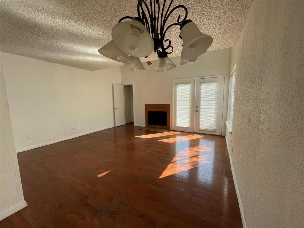 9811 Walnut Street, Unit F207 Dallas, TX 75243 - Photo 2 of 12 Unfurnished living room with dark wood-style flooring, a textured ceiling, a textured wall, a fireplace with flush hearth, and a chandelier