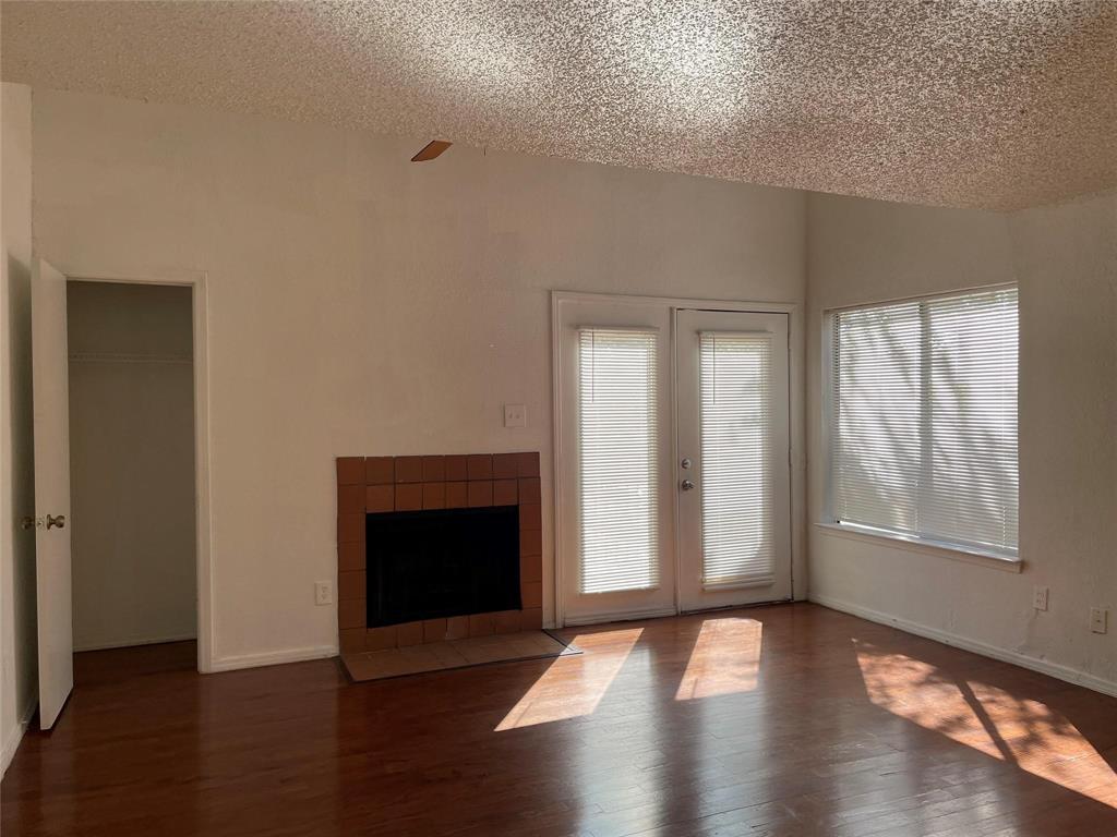 9811 Walnut Street, Unit F207 Dallas, TX 75243 - Photo 3 of 12 Unfurnished living room featuring a textured ceiling, dark wood-type flooring, french doors, a fireplace, and ceiling fan