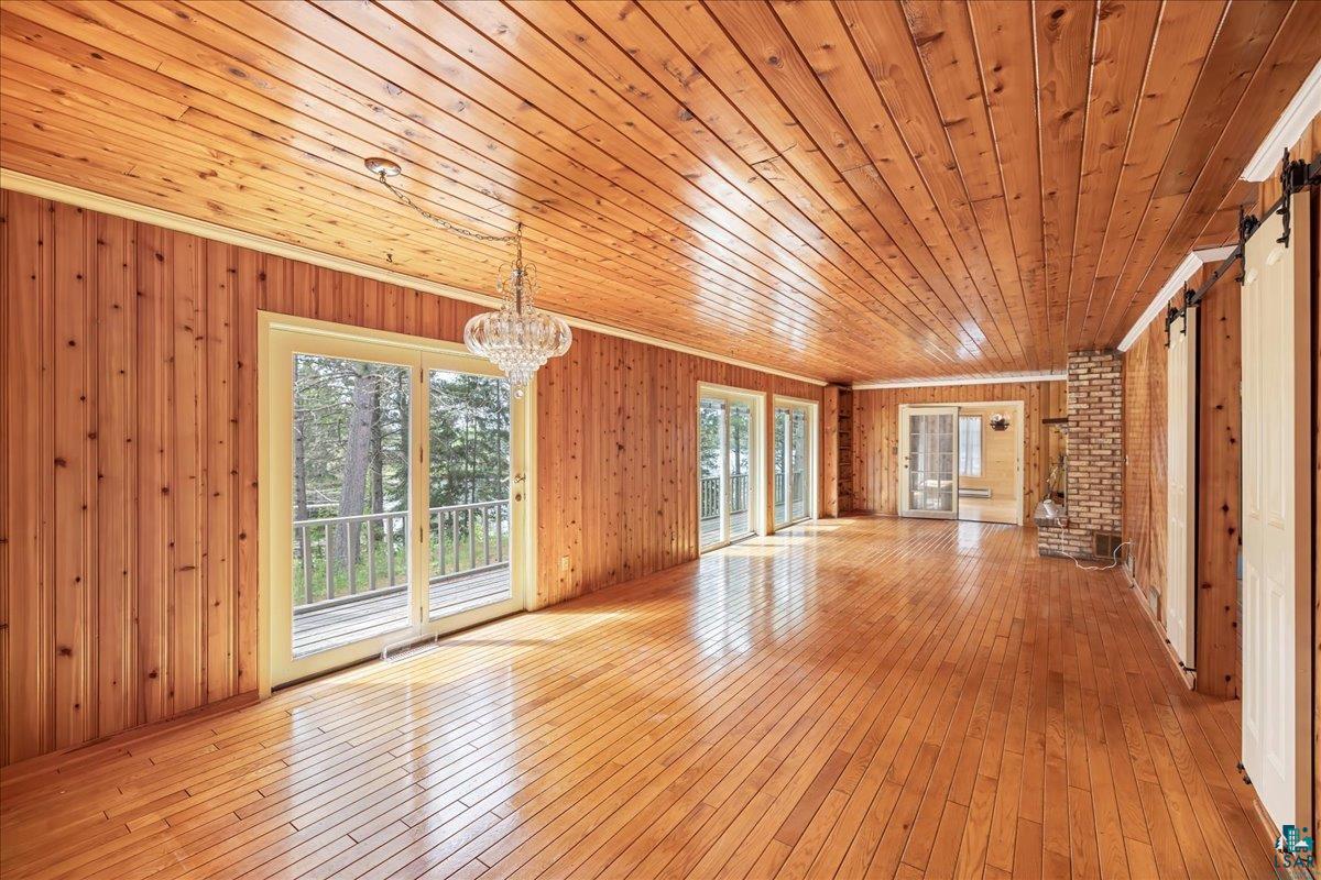 1804 North Bay Road Ely, MN 55731 - Photo 12 of 37 Unfurnished living room with wood ceiling, wooden walls, brick wall, and light hardwood / wood-style flooring