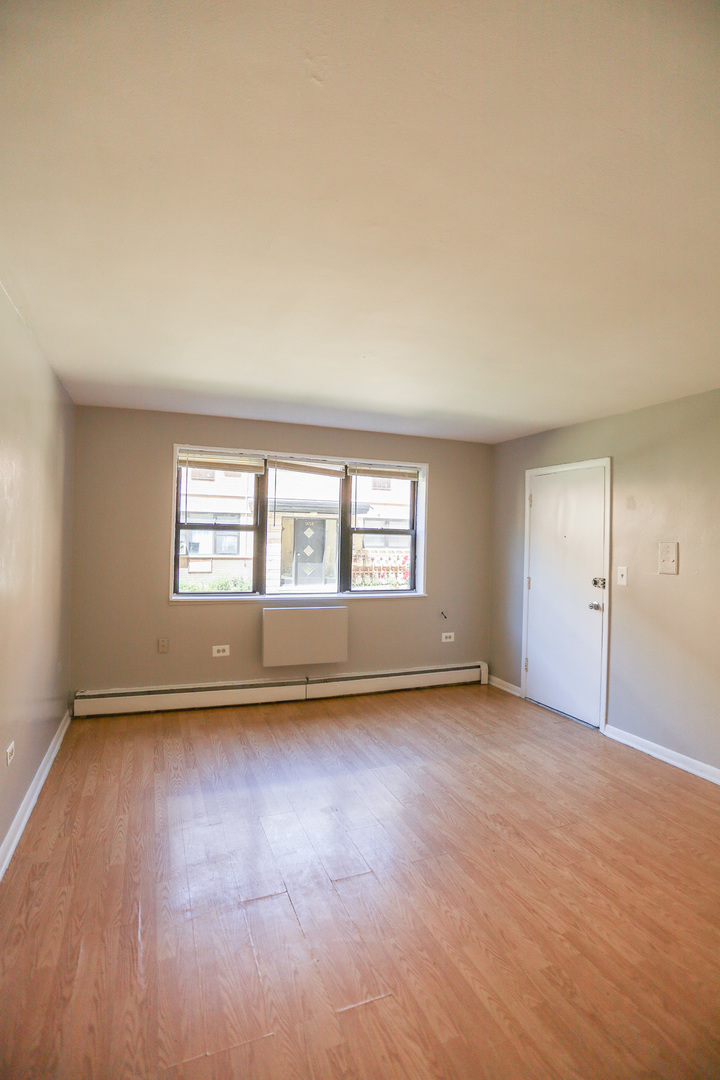 1654 West Pratt Boulevard, Unit 1S Chicago, IL 60626 - Photo 4 of 7 an empty room with wooden floor and windows