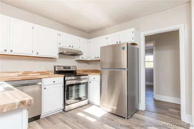 a kitchen with stainless steel appliances granite countertop a refrigerator a stove a sink and white cabinets with wooden floor