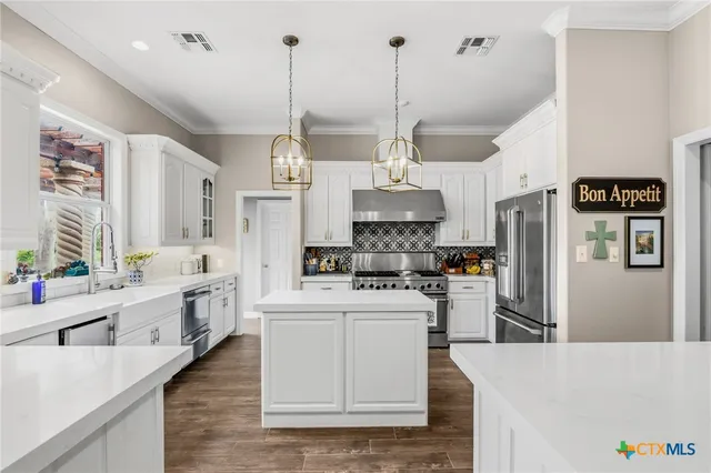 a large white kitchen with granite countertop a sink white cabinets and wooden floor