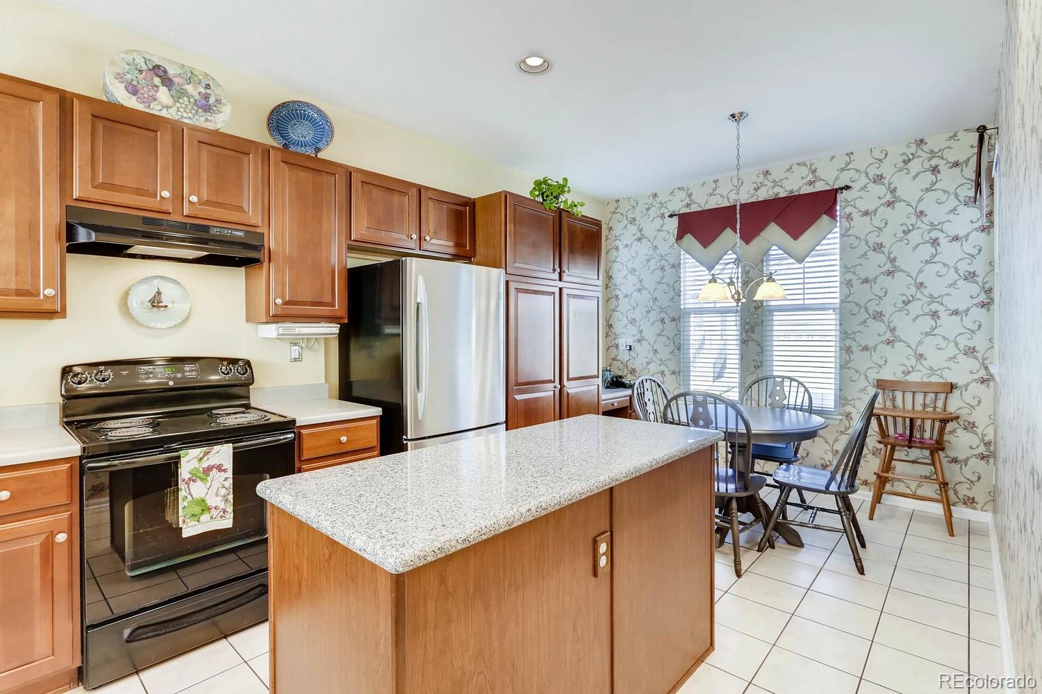 10825 Towerbridge Road Highlands Ranch, CO 80130 - Photo 10 of 24 a kitchen with stainless steel appliances kitchen island granite countertop a table chairs and a refrigerator