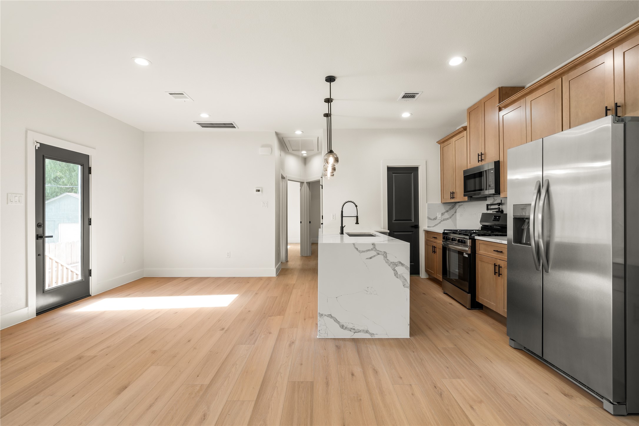 5321 Rue Street Houston, TX 77033 - Photo 7 of 23 Gourmet kitchen setup — statement waterfall island with undermount sink, pot filler over gas range, stainless steel appliances, and custom warm wood cabinetry.