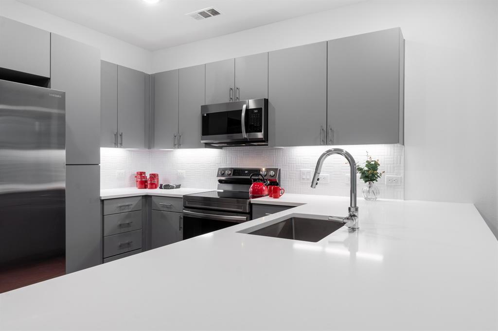 4801 Springdale Road, Unit 2010 Austin, TX 78723 - Photo 5 of 28 Kitchen featuring gray cabinetry, stainless steel appliances, light stone counters, modern cabinets, and decorative backsplash