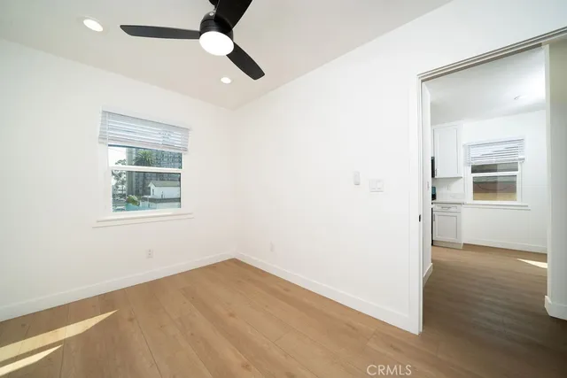 an empty room with wooden floor chandelier fan and windows