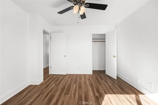 an empty room with wooden floor ceiling fan and windows