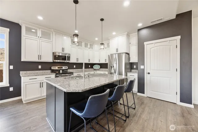 a kitchen with stainless steel appliances granite countertop a sink a stove a refrigerator cabinets and chairs