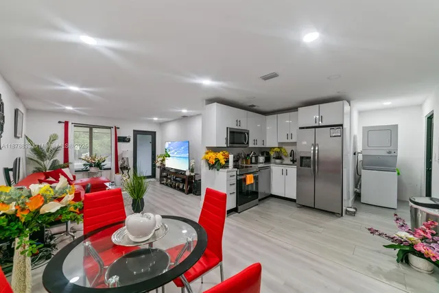 a living room with stainless steel appliances furniture wooden floor and a kitchen view