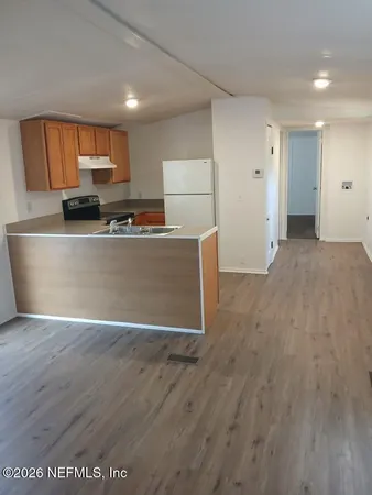 a living room with stainless steel appliances wooden floors and kitchen view