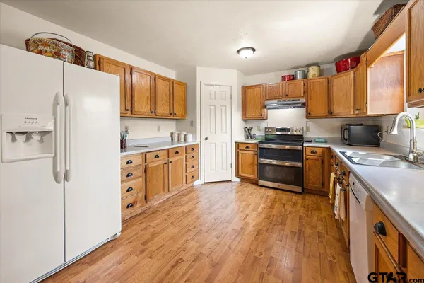 a kitchen with stainless steel appliances granite countertop a refrigerator a stove top oven a dining table and chairs with wooden floor
